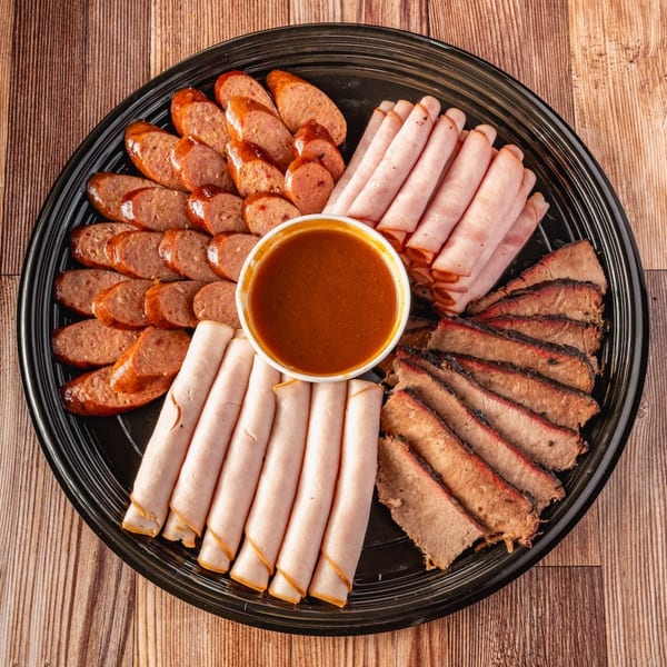 Bowie Barbeque platter with sliced sausage, rolled ham, brisket, and a bowl of BBQ sauce.