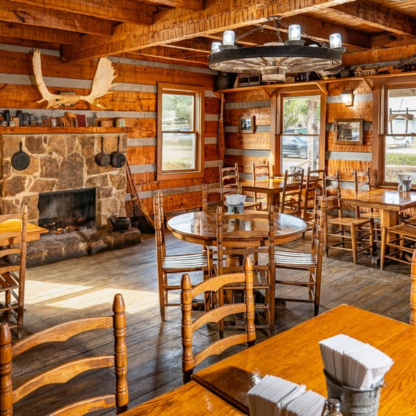 Rustic Bowie Barbeque dining room with wooden tables, chairs, stone fireplace, and wagon wheel chandelier.