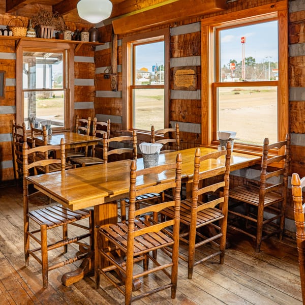 Rustic Bowie Barbeque dining room with wooden tables and chairs, log walls, and sunny windows.