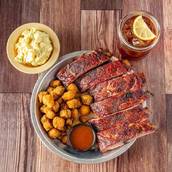 Bowie Barbeque ribs, fried okra, potato salad, and iced tea with lemon on a wooden table.
