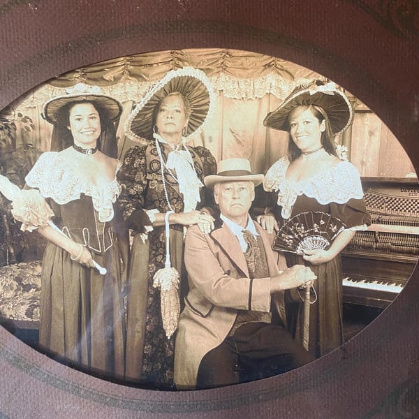 Sepia-toned photo of two women and a man in period costumes, with a piano in the background.