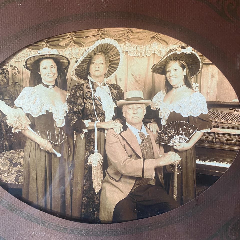 Sepia-toned photo of two women and a man in period costumes, with a piano in the background.