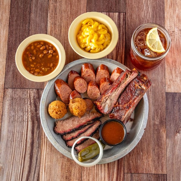 Bowie Barbeque platter with ribs, sliced brisket, sausage, hushpuppies, baked beans, mac and cheese, and iced tea.