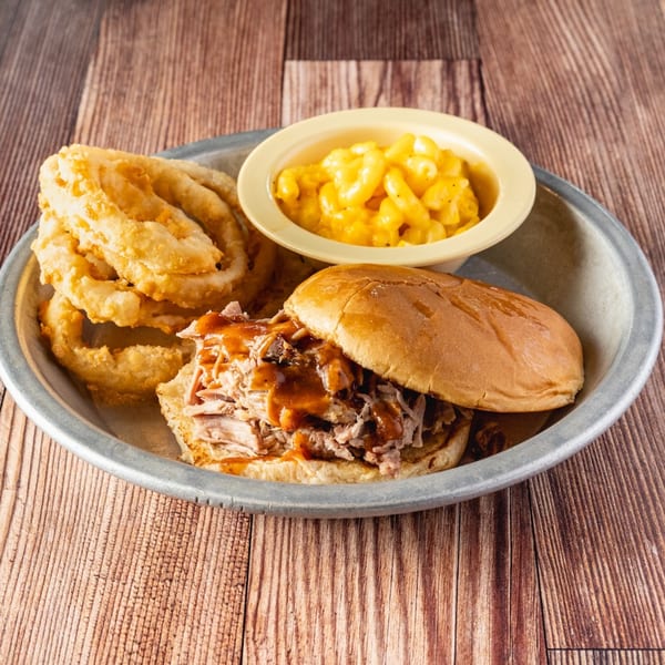 Bowie Barbeque pulled pork sandwich with onion rings and macaroni and cheese on a metal plate.